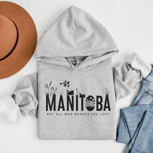 Featuring a serene prairie landscape, the design captures the essence of the heartland with wildflowers and prairie grasses growing out of the letters Manitoba.